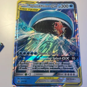 Magikarp & Wailord GX Pokémonkort - Säljer ett Magikarp & Wailord GX TAG TEAM Pokémonkort med 300 HP. Kortet har en holografisk yta och visar en episk scen med Magikarp och Wailord i vattnet. Perfekt för samlare eller spelare som vill stärka sin kortlek.