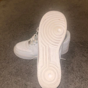 Vita Nike Air Force 07 - Säljer ett par klassiska vita Nike Air Force sneakers. De har en stilren design med snörning och perforerade detaljer på tån för extra ventilation. Perfekta för en avslappnad och sportig look.