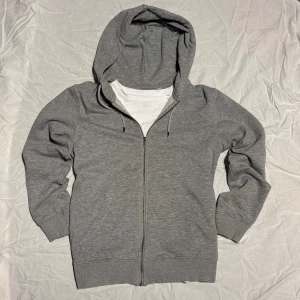 Grå hoodie från Jack & Jones - Säljer en stilren grå hoodie från Jack & Jones. Den har en dragkedja framtill och en bekväm huva med snörning. Perfekt för en avslappnad look.