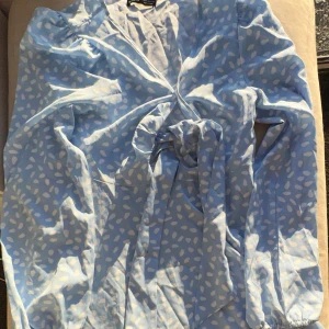 Blå klänning med vita prickar från Shein - Säljer en söt blå klänning med vita prickar från Shein. Klänningen har en knytning framtill och långa ärmar. Perfekt för en somrig look!