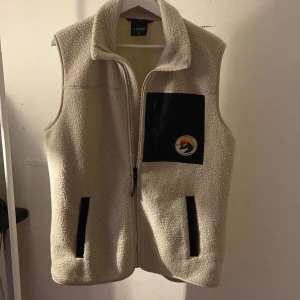 Beige fleeceväst från Everest - Säljer en beige fleeceväst från Everest med dragkedja och en praktisk bröstficka med märke. Perfekt för kyliga dagar och enkel att matcha med andra plagg.