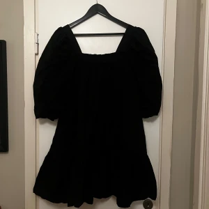 Svart klänning med puffärmar - Snygg svart klänning med puffiga trekvartsärmar och en fyrkantig urringning. Perfekt för en stilren look. Klänningen har en volangdetalj vid fållen.