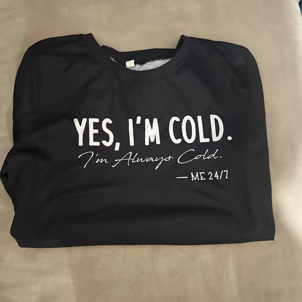 Säljer en svart långärmad tröja med trycket 'YES, I'M COLD. I'm Always Cold. - ME 24/7'. Perfekt för dig som alltid fryser! 🖤. Neuletakit & Villapaidat.