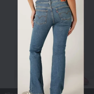 Blå jeans från Levi's - Snygga blå Levi's jeans med klassisk femficksdesign och knappgylf. De har en bootcut-stil som ger en avslappnad look. Perfekta för en casual outfit. Modellen heter superlow boot!