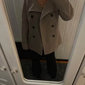 Beige kappa från H&M - Säljer en stilren beige kappa från H&M med dubbelknäppning och bred krage. Perfekt för höst och vår. Kappan har långa ärmar och en klassisk design som passar till många olika stilar.