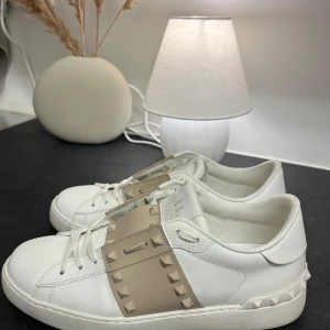 Valentino opens - Snygga vita sneakers från Valentino med beige detaljer och nitar. Skorna har en stilren design med snörning och en bekväm passform. Perfekta för att ge din outfit en lyxig touch.