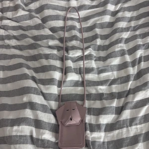 Rosa axelväska från Zara - Säljer en stilren rosa axelväska från Zara. Väskan har en minimalistisk design med en lång rem och ett litet fack framtill. Perfekt för att bära med sig det viktigaste på ett smidigt sätt.
