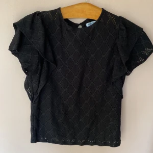 Snygg svart blus från Holly & Whyte S - Holly & Whyte /Lindex top med ett diskret mönster och volangdetaljer på ärmarna. Perfekt för en stilren look. Knappt använd 