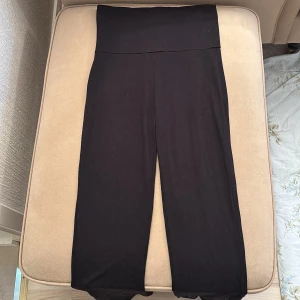 Svarta byxor - Svarta byxor med hög midja som går att dra ner för en snygg detalj. Byxorna är tillverkade i ett mjukt material som ger en bekväm känsla. Använd flertal gånger men är i acceptabelt skick.