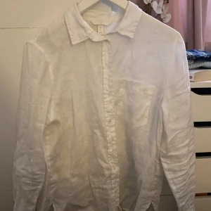 Vit linneskjorta - Säljer en stilren vit linneskjorta med klassisk krage och knappar framtill. Skjortan har en bröstficka och långa ärmar, perfekt för en avslappnad men ändå uppklädd look. Använd 1 gång!🫶🏻