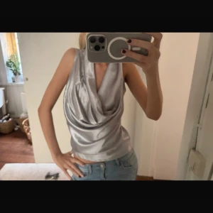 Silverfärgad ärmlös topp - Snygg och glansig silverfärgad topp med draperad halsringning. Perfekt för en kväll ute eller en speciell tillställning. Toppen är ärmlös och har en elegant look.