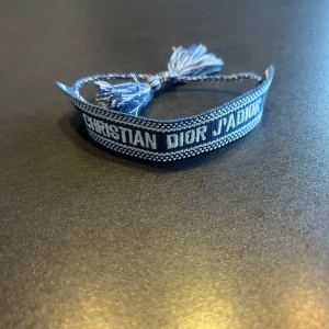 Dior armband - Snyggt blått armband från Christian Dior. Armbandet har en flätad design  med tofsar i ändarna, vilket ger en bohemisk touch. Perfekt för att lägga till en stilfull detalj till din outfit. Hör gärna av er vid frågor och funderingar👍🙌