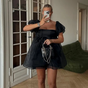 Svart offshoulder klänning från NA-KD - Trendig svart offshoulder klänning från NA-KD med puffiga ärmar och en stor rosett i ryggen. Klänningen har en luftig och voluminös design som ger en elegant look. Perfekt för att sticka ut på festen! I stl 32 men passar mig som XS🥰