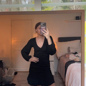 Svart klänning med volangdetaljer - Snygg svart klänning med v-ringning och långa ärmar. Klänningen har en volangdetalj vid fållen som ger en extra touch. Perfekt för festligare tillfällen! Aldrig använd så i toppen skick!