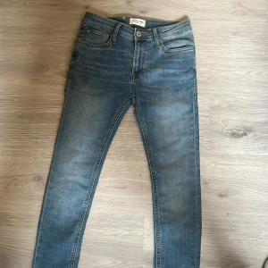 Blå jeans från Jack & Jones - Snygga blå jeans från Jack & Jones med en klassisk femficksdesign. De har en knappgylf och är i en slim passform som ger en modern look. Perfekta för en avslappnad stil.