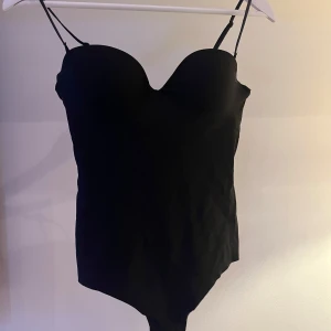 Svart body från H&M - Snygg svart body från H&M med avtagbara axelband och lätt formande effekt. Perfekt för en stilren look. Bodyn har en elegant design med en liten öppning i ryggen. Slutsåld och hög efterfrågan därav priset!🥰