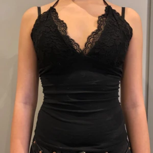 Svart spetslinne - Snyggt svart linne med spetsdetaljer och halterneck. Dömmer har gått upp lite på bandet. 