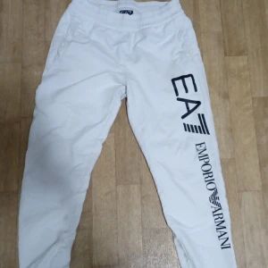 Vita mjukisbyxor från Emporio Armani - Snygga vita mjukisbyxor från Emporio Armani med EA7-logga i svart på benet och bakfickan. Byxorna har en elastisk midja för extra komfort och en avslappnad passform. Perfekta för en stilren och bekväm look.