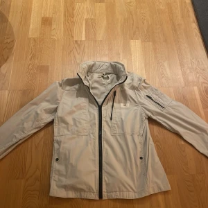Beige jacka från G-Star RAW - Säljer en stilren beige jacka från G-Star RAW. Jackan har en dragkedja framtill och flera praktiska fickor, inklusive en på ärmen. Perfekt för en casual look. Jackan har en inbyggd luva som man kan dra ut när man vill.