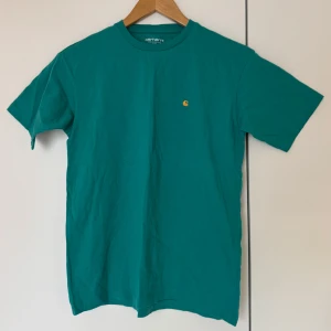 Turkos t-shirt från Carhartt - Turkos t-shirt från Carhartt med en liten guldig logga på bröstet. 