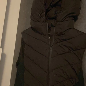 Svart dunjacka från Zara - Säljer en svart dunjacka från Zara med huva och dragkedja. Jackan har en quiltad design och är perfekt för kyligare väder. Den är stilren och enkel att matcha med olika outfits.