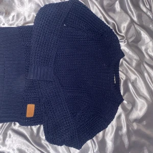 Mörkblå stickad tröja från Weather Report - Säljer en snygg mörkblå stickad tröja från Weather Report. Tröjan har en klassisk design med ribbade muddar och en liten läderdetalj på framsidan. Perfekt för kyligare dagar. Passar bra till både jeans och kjol.