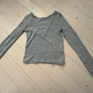 Grå långärmad tröja med snörning - Säljer en stilren grå långärmad tröja med snygg snörning i ryggen. Perfekt för en casual look och passar bra till jeans eller kjol. Tröjan är mjuk och bekväm, vilket gör den idealisk för både höst och vår.