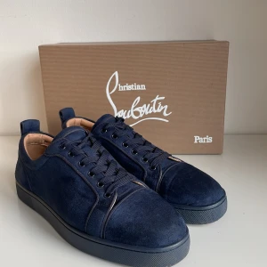 Mörkblå sneakers från Christian Louboutin - Snygga mörkblå sneakers i mocka från Christian Louboutin med den ikoniska röda sulan. Skorna har snörning och en stilren design som passar perfekt för en trendig look. Hör av er vid frågor!