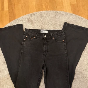 Svarta bootcut jeans från Zara - Snygga svarta bootcut jeans från Zara med klassisk femficksdesign och knappgylf. Perfekta för en trendig look med sin vida passform nedtill. Tillverkade i ett bekvämt material som ger en skön känsla hela dagen.