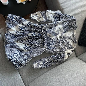 Mönstrad klänning från Zara - Snygg mönstrad klänning från Zara i vitt och marinblått. Klänningen har långa ärmar och ett knytbälte i midjan för en fin passform. Perfekt för en stilfull look med sitt unika mönster.