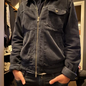 Mörkblå manchesterjacka från Morris - Säljer en snygg mörkblå manchesterjacka från Morris. Jackan har en dragkedja framtill och en bröstficka med knapp. Den är långärmad och har en klassisk krage. Perfekt för en stilren look.