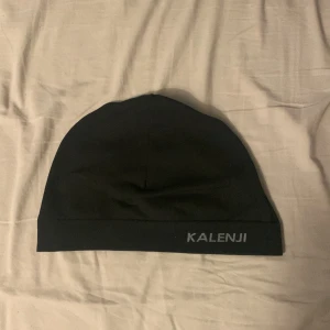 Svart mössa från Kalenji - Säljer en svart mössa från Kalenji. Perfekt för löpning eller andra utomhusaktiviteter. Enkel design med Kalenji-logga på kanten. Tillverkad i ett mjukt och bekvämt material.