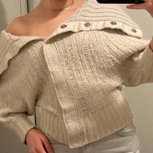 Beige stickad tröja från Guess Jeans - Säljer en snygg beige stickad tröja från Guess Jeans. Tröjan har en  offshoulder-design med stora knappar på kragen. Går att justera halsringningen beroende på hur man knäpper💞