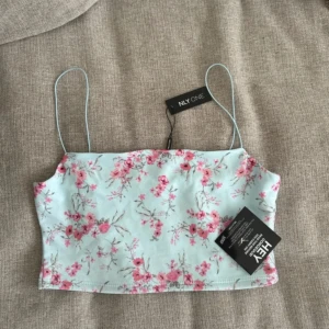 Blommig linnetopp från NLY One - Söt ljusblå linnetopp med rosa blommönster från NLY One. Toppen har tunna axelband och en croppad passform, perfekt för varma sommardagar. Ett måste i garderoben för en fräsch och somrig look! M men passar S 
