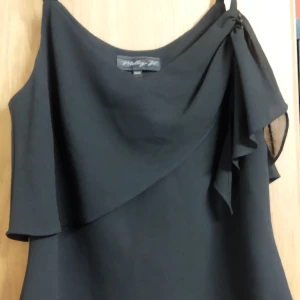 Svart ärmlös topp från Molly Jo - Snygg svart ärmlös topp från My Way med dubbla lager och asymmetrisk design. Perfekt för en stilren look. Tillverkad i ett lätt och luftigt material som ger en elegant känsla.