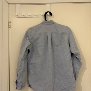 Blå skjorta från Ralph Lauren - Snygg blå skjorta från Ralph Lauren med klassisk krage och knappar framtill. Skjortan har långa ärmar och en broderad logga på bröstet. Perfekt för en stilren look!