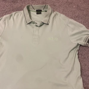 Ljusgrön pikétröja från Boss - Snygg ljusgrön pikétröja från Boss med klassisk krage och korta ärmar. Tröjan har en diskret logga på bröstet och kontrasterande detaljer på kragen. Perfekt för en stilren look.storlek m