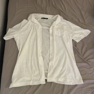 Vit frottéskjorta från 157 - Säljer en vit kortärmad skjorta i frotté från 157. Skjortan har knappar framtill och en bröstficka. Perfekt för en avslappnad stil.