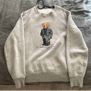 Grå sweatshirt från Ralph Lauren med björnmotiv - en grå sweatshirt från Ralph Lauren med björnmotiv på framsidan. Väldigt bra skick köpt på Plick. Pris kan diskuteras