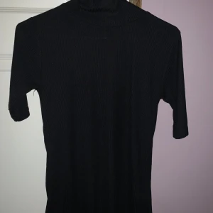 Svart ribbad polotröja - Säljer en stilren svart ribbad polotröja i storlek XS. Tröjan har korta ärmar och en klassisk polokrage, perfekt för en elegant look. Passar bra till både jeans och kjol. Pris: 149 kr.