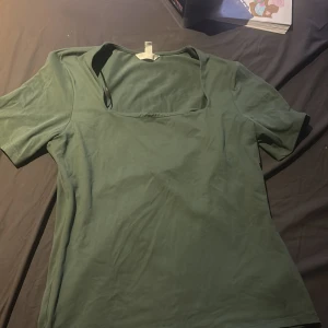 Grön topp från H&M - Säljer en stilren grön topp från H&M. Toppen har korta ärmar och en fyrkantig halsringning, vilket ger en modern look. Perfekt för en avslappnad stil.
