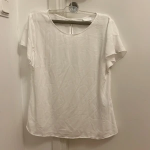 Vit blus från Vila - Säljer en stilren vit sommarblus från Vila i storlek M. Blusen har korta ärmar med en lätt volangdetalj och en rund halsringning. Perfekt för en elegant och luftig look. 🕊️Den är aldrig använd. Kan tänka mig gå ner i pris vid snabb affär 🫶
