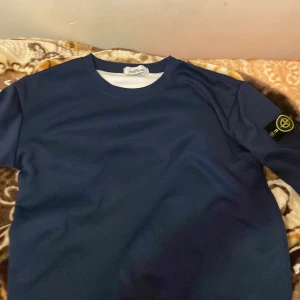 Mörkblå tröja från Stone Island - Säljer en stilren mörkblå tröja från Stone Island med deras ikoniska märke på ärmen. Tröjan har en rund halsringning och är perfekt för en avslappnad look. Passar bra till både jeans och chinos.