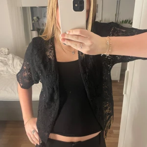 Svart spetsbolero - Säljer en elegant svart bolerotopp i spets. Den har korta ärmar och en öppen design framtill. Perfekt för att lägga till en touch av stil till din outfit.
