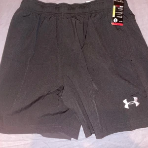 Svarta träningsshorts från Under Armour - Snygga svarta träningsshorts från Under Armour i nyskick. I detta fall är jag inte helt säker på att dom är äkta då jag fick dom som en julklapp av en släkting. Jag har redan ett liknande par så därför säljer jag dessa. Om jag får gissa så är dom äkta då det inte finns något som tyder annat. 