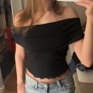 Svart offshoulder topp - Snygg svart offshoulder topp med en elegant design. Toppen har en croppad stil och är perfekt för en trendig look. Den är tillverkad i ett mjukt och luftigt material, den har en fin kantdetalj längst ner.