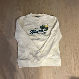 Vit sweatshirt från Morris - Säljer en stilren vit sweatshirt från Morris med tryck på framsidan. Tröjan har långa ärmar och en rund halsringning. Perfekt för en avslappnad stil. 