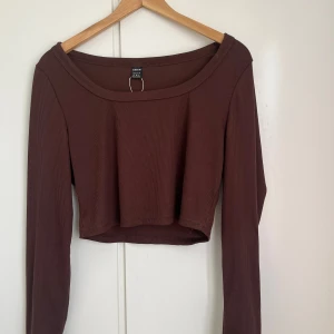 Brun ribbad croppad topp - Säljer en brun ribbad croppad topp med långa ärmar. Perfekt för en stilren och avslappnad look. Toppen har en rund halsringning och är gjord i ett mjukt material.