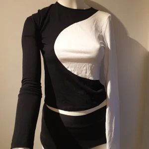 Svart och vit långärmad topp från NA-KD - Snygg långärmad topp från NA-KD i svart och vitt med ett unikt asymmetriskt mönster. Perfekt för att ge en stilren touch till din outfit. Tillverkad i Turkiet.