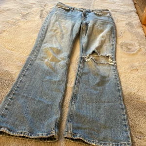 Blå jeans med utsvängda ben - Säljer ett par blå jeans från G Perfect Jeans med utsvängda ben och en sliten detalj på ena benet. Perfekta för en avslappnad stil.